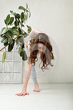 Young yogini practicing in a room with white walls and plant