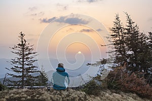 A young youth in headphones watches the sunrise in the mountains with a cup of tea, a sonception, a trip, a hike, a rest, solitude