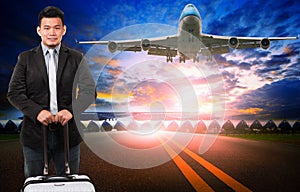 younger asian man and traveling luggage standing against passenger plane flying over airport runway