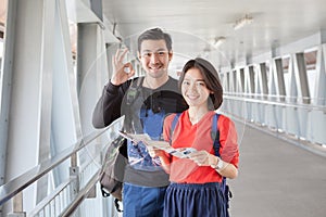 younger asian traveling man and woman standing with toothy smiling face sigh all right by okay hand sue for modern people