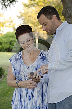 Younger man helping senior woman with her smart phone.