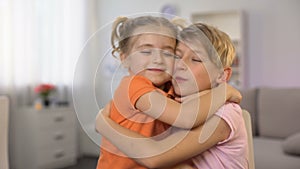 Younger sister hugging brother drawing at table, kissing cheeks each other, love