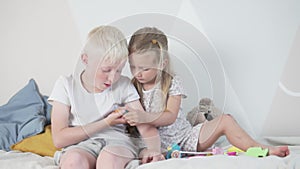 The younger sister measures the older brother`s temperature with a toy thermometer.