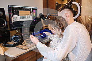 Younger sister sits on brothers knees and put finger on keyboard with neon light. Little girl help brother work on