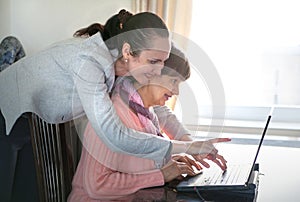 Younger woman helping an elderly person using laptop