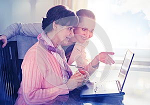 Younger woman helping an elderly person using laptop computer for internet search.