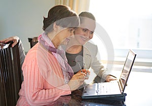 Younger woman helping an elderly person using laptop computer for internet search.
