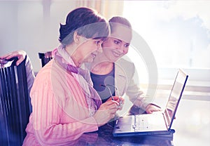 Younger woman helping an elderly person using laptop computer for internet search.