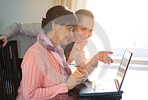 Younger woman helping an elderly person using laptop computer for internet search. Young and pension age generations working