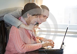Younger woman helping an elderly person using laptop computer for internet search. Young and pension age generations working