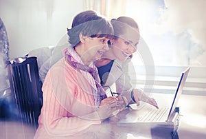 Younger woman helping an elderly person using laptop