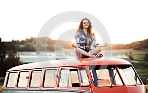 A young girl on a roadtrip through countryside, sitting on the roof of minivan doing yoga. photo