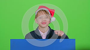 Youngster boy appeared from behind a blue poster points to his index fingers. Green screen