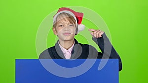 Youngster boy appeared from behind a blue poster points to his index fingers. Green screen. Slow motion