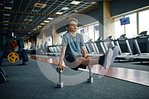 Youngster doing exercise with dumbbells in gym