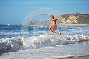 Youngster enjoys a beach run and jump among foamy strong waves