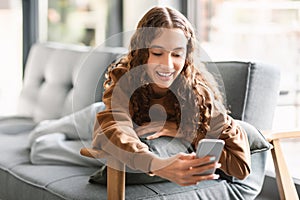 youngster girl using phone for communication relaxing on sofa indoor