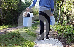 Youngster is holding Plastic bucket on the forest path for plastic bottles and trash