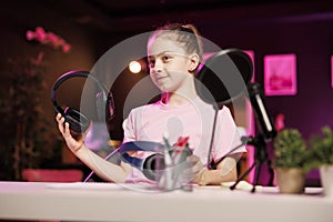 Youngster presents headphones in different price ranges to audience, filming in neon lit home studio