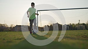 Youngster run with soccer ball, across the green field near football goal.