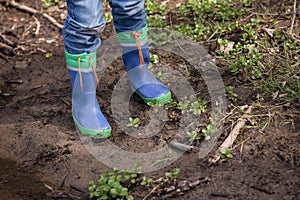 Youngster is standing in a mud with his rainboots.