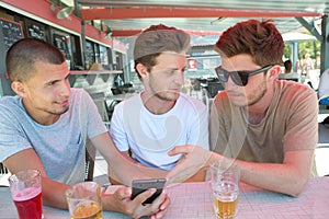 Youngsters at bar watching photos on mobile phone