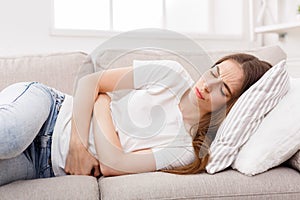 Young girl suffering from stomachache lying down on sofa photo