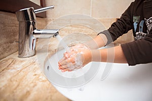 Younk kid washing his hands and rinsing off soap under tap water