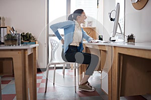 Your body is telling you something. a young businesswoman experiencing back pain while working at her desk in a modern