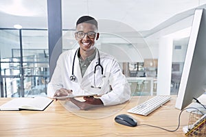 Your health is my top priority. a handsome young doctor sitting alone in his office at the clinic and using his digital