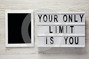 `Your only limit is you` word on modern board, tablet with blank screen on a white wooden background, top view. From above, flat