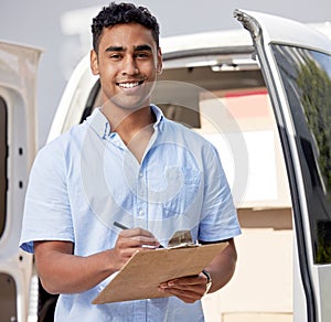 Your package is on my list. Portrait of a young delivery man writing on a clipboard while loading boxes from a van.