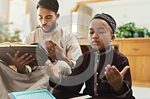 Your prayers for your children are the greatest legacy. a young muslim man and his son reading in the lounge at home.