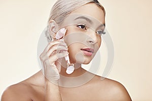 Your skin will thank you. Studio shot of a young woman using a jade derma roller on her face.