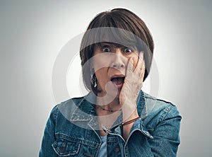 Your story is sending shocks through me. Studio portrait of a senior woman looking shocked against a grey background.