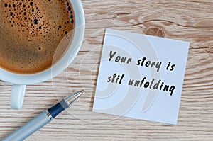 Your Story Is Still Unfolding motivation inscription at notepad near morning cup of coffee, Top view with empty space photo