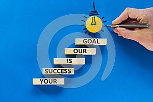 Your success is our goal symbol. Wooden blocks with words Your success is our goal. Light bulb icon. Businessman hand, pen. Blue