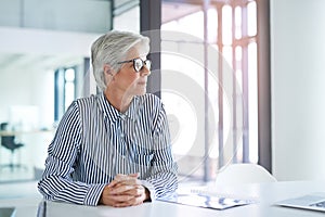 Your thoughts govern your future. an attractive mature businesswoman looking out of a window while sitting at her office