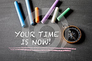 Your time is now. Compass and colorful pieces of chalk on blackboard background
