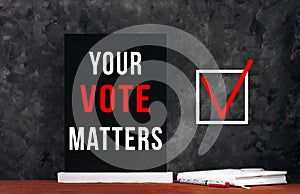 Your Vote Matters text sign on black chalkboard with white notebok and red pen on dark background. Make political choice