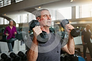 Your willpower is all that matters not age. a senior man working out with weights at the gym.