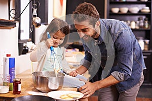 Youre doing great sweetheart. A cute little girl helping her dad make pancakes at home.