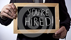 Youre hired with exclamation written on blackboard, businessman holding sign