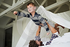 Youre my superhero. Cropped shot of a young man holding his son up like a superhero while playing on the bed.