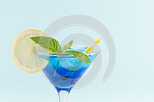 Youth fresh alcohol blue Hawaii cocktail with licor curacao, ice cube, lemon slice, yellow straw in wine glass on mint background. photo