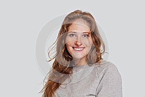 Youth and happiness. Close up portrait of beautiful happy woman with long ginger hair and freckles, dressed casually on white wall