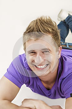 Youth Lifestyle Concept: Closeup Portrait of Smiling Tanned Caucasian Handsome Man Laying on Floor With Folded Hands