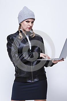 Youth Lifestyles. Caucasian Blond Femalr in Warm Hat and Leather Jacket Posing With Laptop With Ingratiating facial Expression on photo