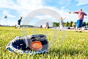 Youth sized glove with a baseball inside sitting on a grass field with players in the background