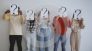 Youth and social problems. Group of young serious diverse people holding question mark cards and hiding faces